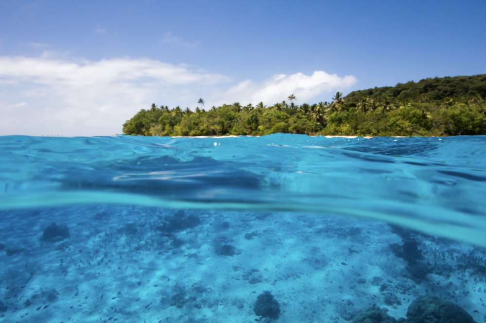 An over-under split shot of a tropical island through perfectly clear turquoise water in The Kingdom of Tonga